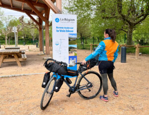 Capucine est descendue de son vélo. Elle regarde le panneau qui indique qu'elle se trouve sur le circuit de la voie bleue, un itinéraire vélo. 