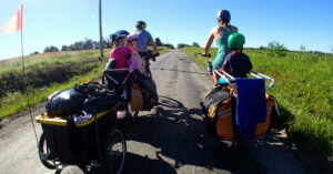 Une famille voyage à vélo avec ses enfants dans des remorques vélos. 