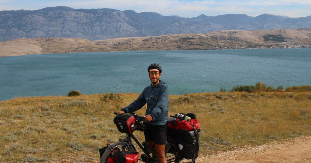 Pierre est auteur du blog En Roue Libre, il est sur son vélo ave des sacoches rouges devant un lac. 