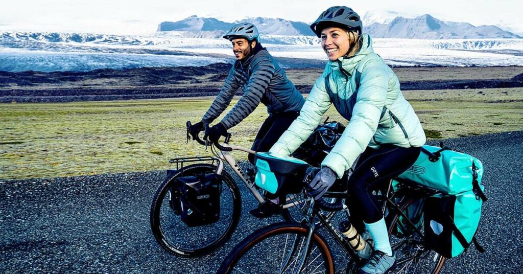 Un couple à vélo, équipé pour le froid avec doudounes et gants et des sacoches pour le cyclotourisme. 