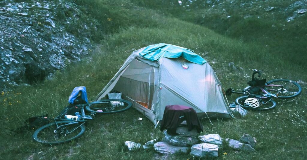 Une tente au milieu de la nature, avec deux vélos couchés au sol de chaque côté. 