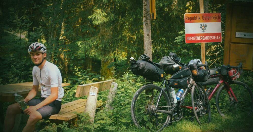 Amaury est assis sur un banc, à côté de son gravel et du panneau qui indique l'entrée sur le territoire de la République Tchèque. 