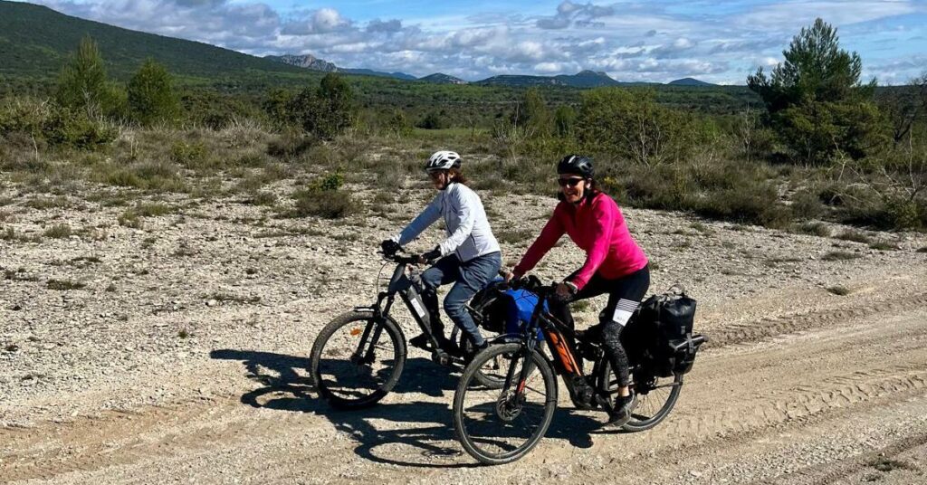 Deux cyclotouristes roulent côte à côte à vélo sur un chemin, autour du Pic Saint Loup. 