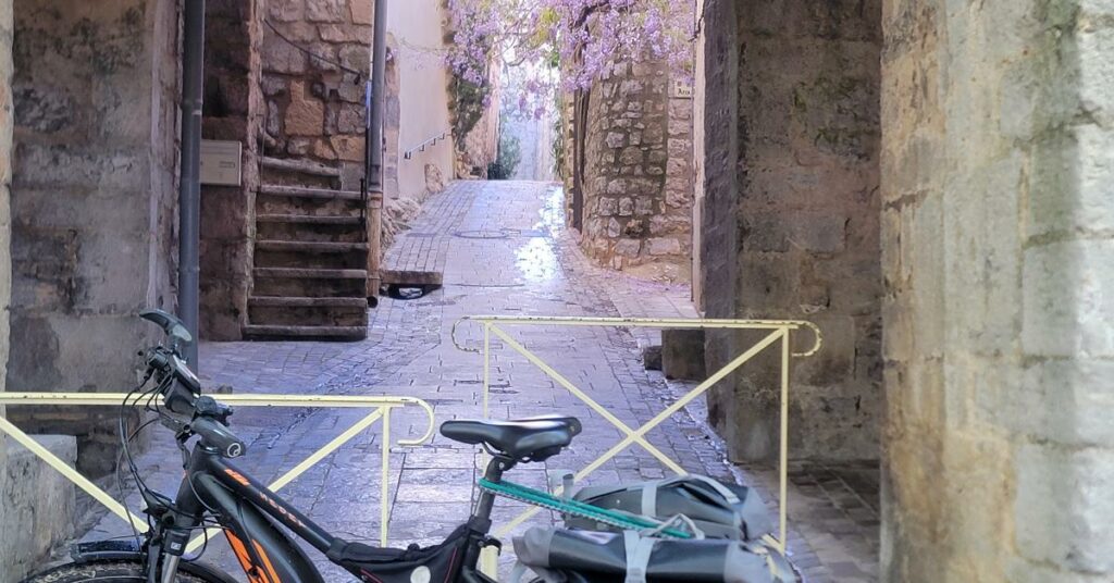 Vue d'une ruelle médiévale avec un vélo au premier plan et une glycine au second plan. 