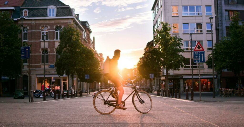 Un homme est à vélo, à l'arrêt et regarde un coucher de soleil en ville. 