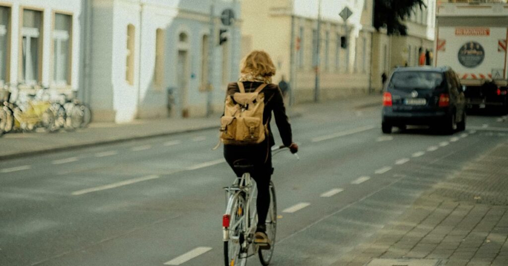 Une femme de dos circule à vélo en ville avec un sac à dos. 