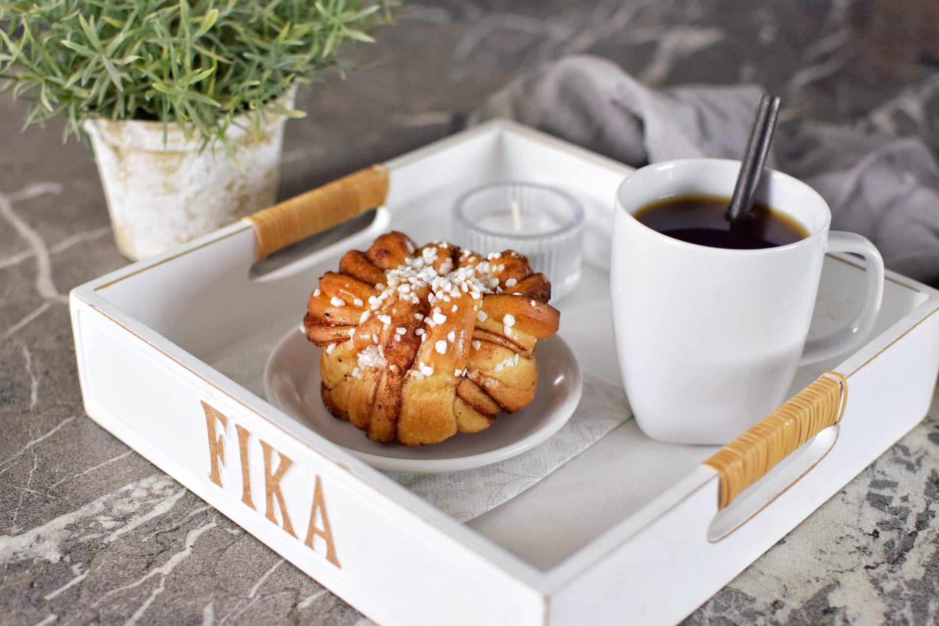 une brioche à la cannelle et une tasse de café posée sur un plateau où est écrit fika