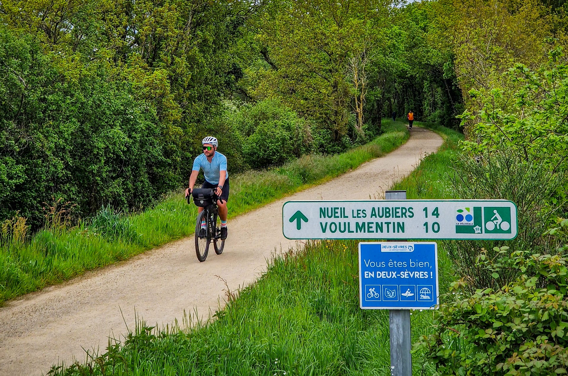 Homme à vélo sur une route de gravel, panneau indiquant arrivée dans les Deux-Sèvres