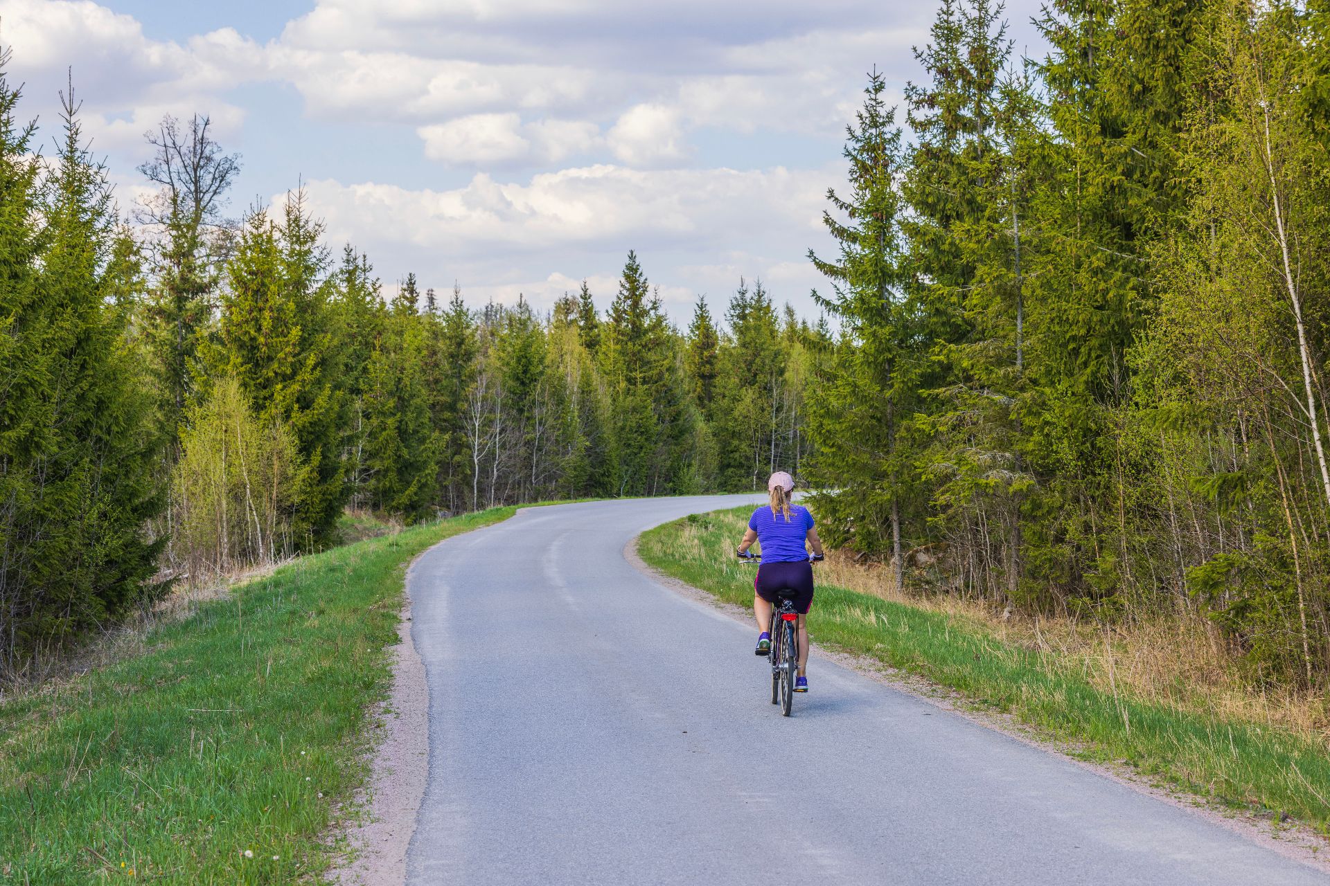 Femme à vélo sur une route entourée de sapins
