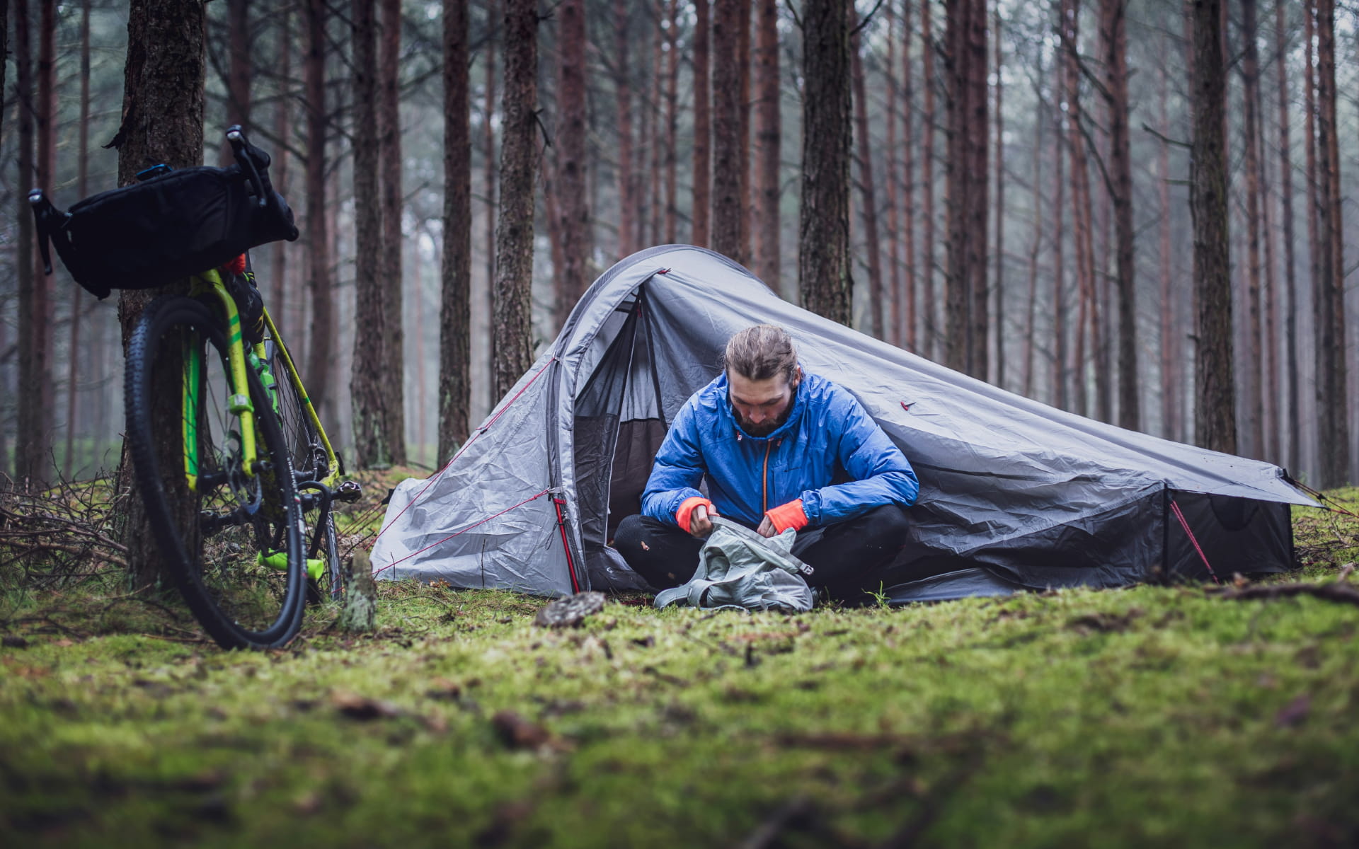 homme devant sa tente dans la forêt avec son vélo à côté