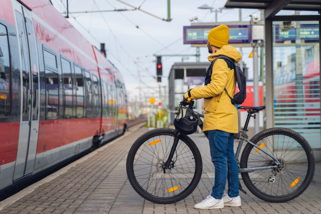 un homme en ciré jaune attend sur le quai pour monter dans le tramway avec son vélo