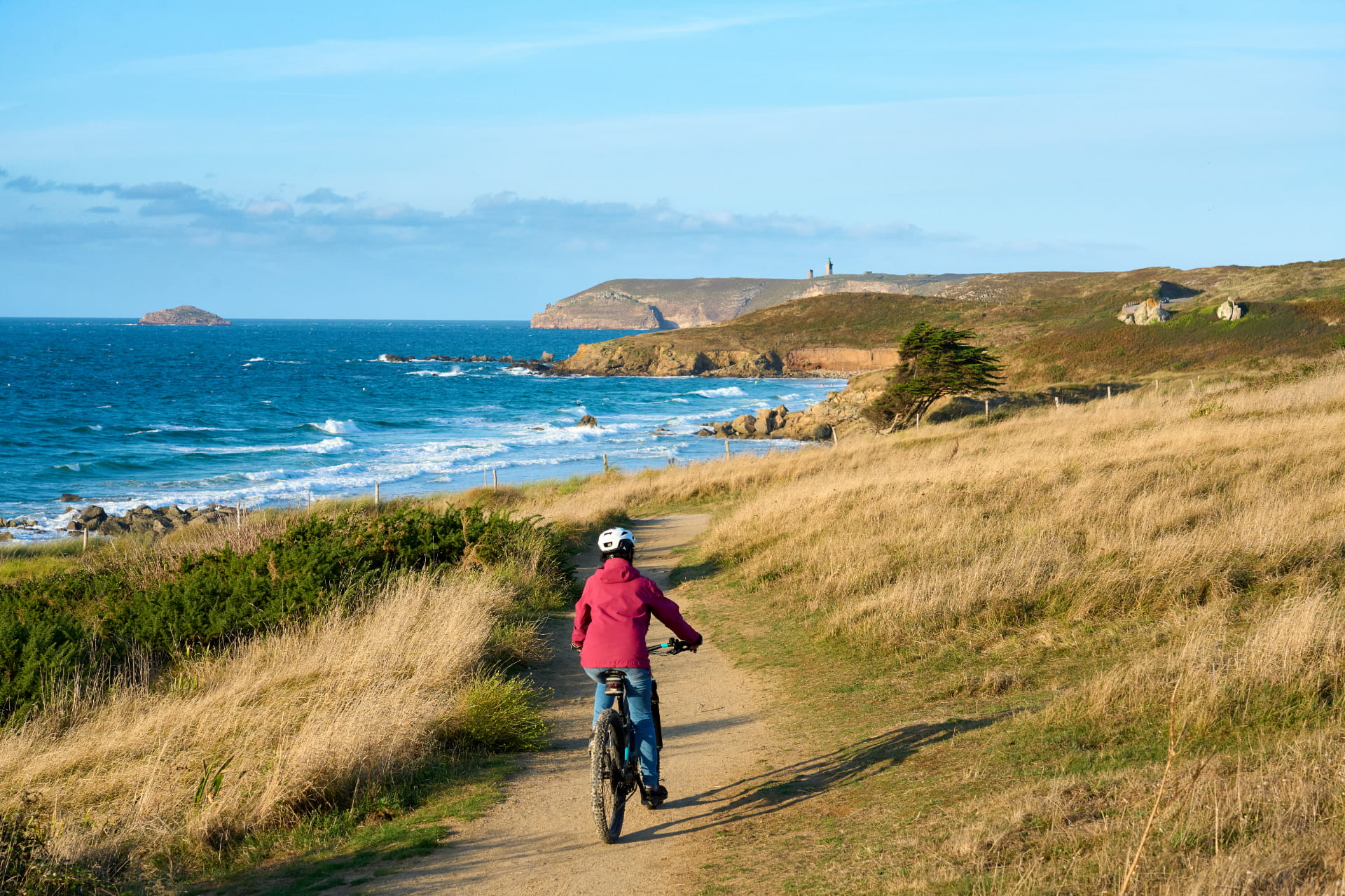 Femme vélo en rouge qui roule face à l'océan en Bretagne