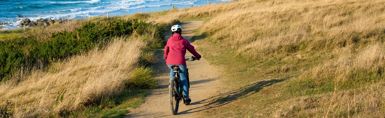 Femme à vélo sur un sentier gravel en face de l'océan en Bretagne